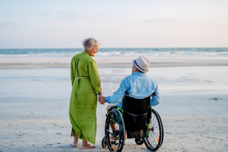 Photo for Senior man on wheelchair enjoying together time with his wife at the sea. - Royalty Free Image