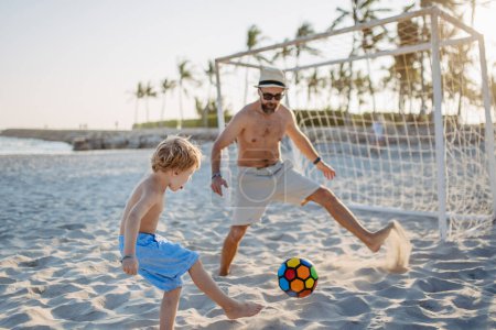 Photo for Father with his son plaing football on a beach. - Royalty Free Image
