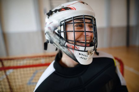 Eine Nahaufnahme der Unihockey-Torhüterin mit Helm, die sich auf ein Spiel in der Sporthalle konzentriert.