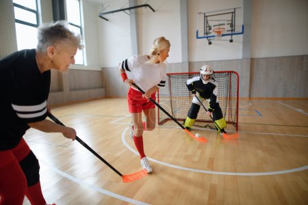 Photo for Multigenerational woman floorball team playing together in gym. - Royalty Free Image