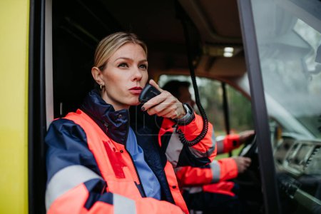 Photo for Portrait of a young woman doctor sitting and talking in to walkie-talkie in ambulance car. - Royalty Free Image