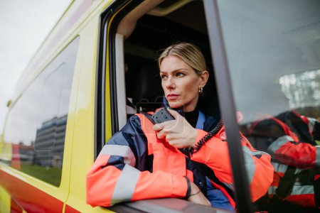 Portrait of a young woman doctor sitting and talking in to walkie-talkie in ambulance car.