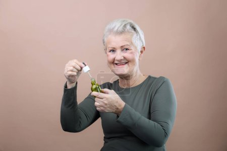 Téléchargez les photos : Portrait of smiling senior woman holding skincare serum drops in bottle.Concept of beauty and skincare. - en image libre de droit