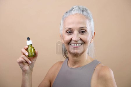 Foto de Portrait of smiling senior woman holding skincare serum drops in bottle.Concept of beauty and skincare. - Imagen libre de derechos
