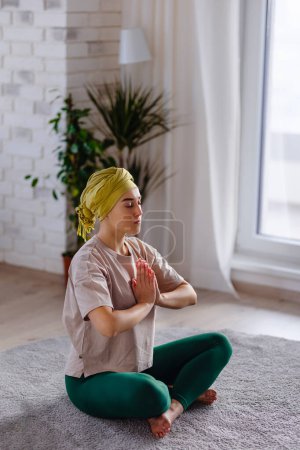 Photo for Young woman with cancer taking yoga and meditating in the apartment. - Royalty Free Image