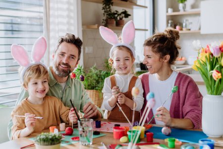 Téléchargez les photos : Famille heureuse avec de petits enfants décorant des œufs de Pâques dans leur maison. - en image libre de droit