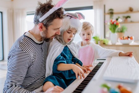 Téléchargez les photos : Enfants heureux en costumes de Pâques jouant sur le piano, avec leur père. - en image libre de droit