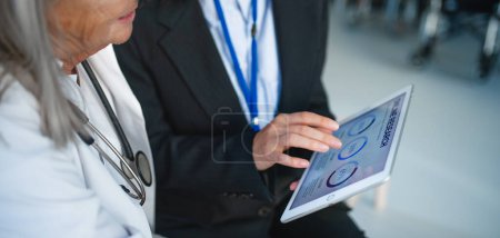 Téléchargez les photos : High angle view of business woman showing chart on digital tablet to doctor in hospital. - en image libre de droit