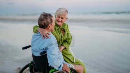 Téléchargez les photos : Homme âgé en fauteuil roulant jouissant ensemble du temps avec sa femme à la mer. - en image libre de droit
