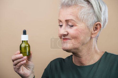 Téléchargez les photos : Portrait of smiling senior woman holding skincare serum drops in bottle.Concept of beauty and skincare. - en image libre de droit