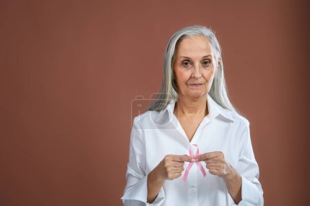Foto de Senior woman holding the pink bow. Breast cancer awareness concept. - Imagen libre de derechos