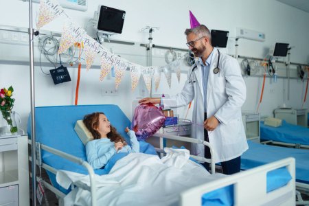 Photo for Happy doctor celebrating birthday with little girl in a hospital room. - Royalty Free Image