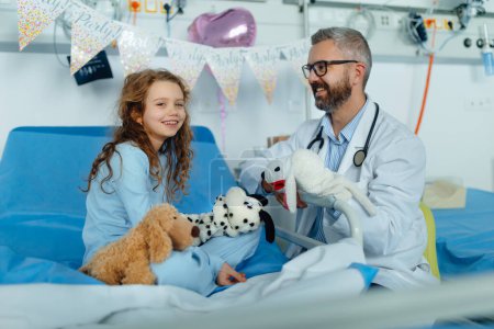 Téléchargez les photos : Joyeux docteur célébrant son anniversaire avec une petite fille dans une chambre d'hôpital. - en image libre de droit
