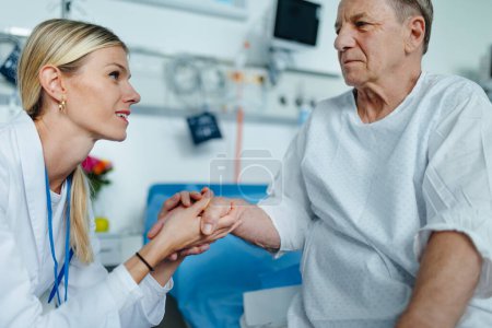 Photo for Young woman doctor holding hand, and talking with her patient in hospital room. - Royalty Free Image