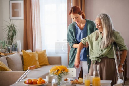 Photo for Nurse helping senior woman with walking after leg injury, in her home. - Royalty Free Image