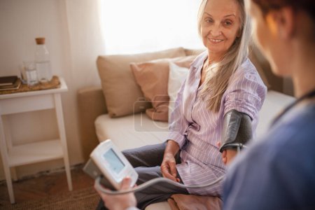 Foto de Enfermera midiendo presión arterial a mujer mayor en su casa. - Imagen libre de derechos