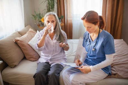 Téléchargez les photos : Infirmière cosultant avec une femme âgée son état de santé et prenant des pilules, à sa maison. - en image libre de droit