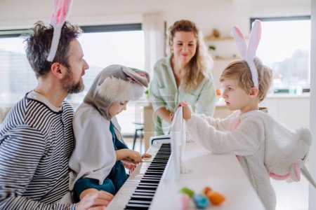 Photo for Happy family with small children in easter costumes playing on the piano. - Royalty Free Image