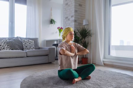 Foto de Mujer joven con cáncer tomando yoga y meditando en el apartamento. - Imagen libre de derechos