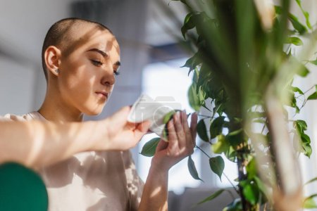 Foto de Young woman with cancer taking care of plants in the apartment. - Imagen libre de derechos