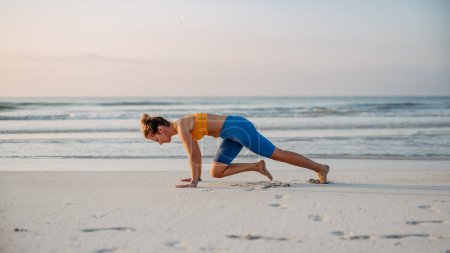 Téléchargez les photos : Jeune femme faisant des exercices à la plage, routine matinale et mode de vie sain concept. - en image libre de droit