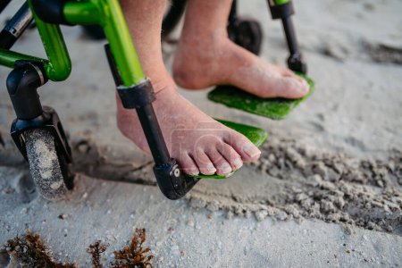 Photo for Close-up of mens feet on wheelchair, on the beach. - Royalty Free Image
