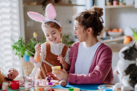 Téléchargez les photos : Happy mother with her little daughter decorating easter eggs in their home. - en image libre de droit