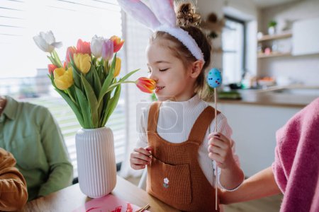 Téléchargez les photos : Little girl smelling bouquet of tulip flowers during decorating the easter eggs with her family. - en image libre de droit