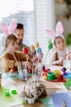 Téléchargez les photos : Père heureux avec de petits enfants décorant des œufs de Pâques dans leur maison. - en image libre de droit