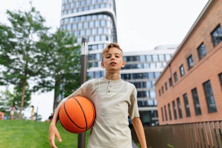 Téléchargez les photos : Cheerful caucasian boy with basketball ball in public city park, looking at camera. - en image libre de droit