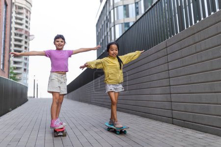 Foto de Cheerful child sitting in skateboard and going down the hill, looking at camera. - Imagen libre de derechos