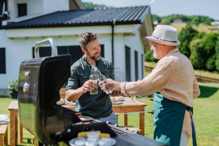 Téléchargez les photos : A senior father with adult son grilling outside on backyard in summer during family garden party. - en image libre de droit