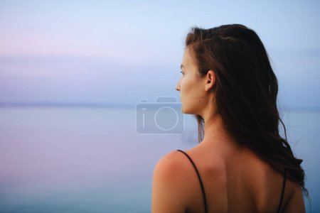 Photo for A rear view of young beautiful sportive girl standing by the lake on early morning and contamplating. - Royalty Free Image