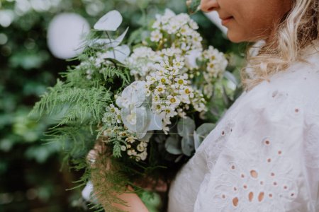 Téléchargez les photos : Un gros plan du bouquet de mariage dans les mains des mariées à la réception à l'extérieur dans la cour arrière - en image libre de droit