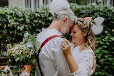 Foto de A mature bride and groom having a romantic moment at wedding reception outside in the backyard. - Imagen libre de derechos
