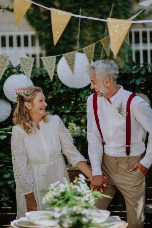 Téléchargez les photos : A mature bride and groom having a romantic moment at wedding reception outside in the backyard. - en image libre de droit
