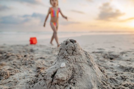 Photo for Little girl playing on the beach, building a sand castle. - Royalty Free Image