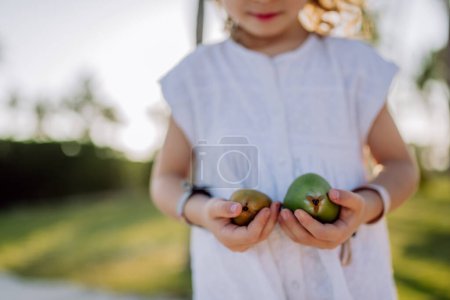 Foto de Little girl posing with an exotic fruit, enjoying time at tropical vacation. - Imagen libre de derechos