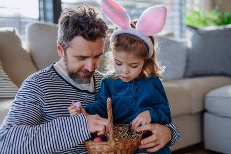 Téléchargez les photos : Petite fille avec des oreilles de lapin tenant panier et montrant des œufs de Pâques père qu'elle a trouvé. - en image libre de droit