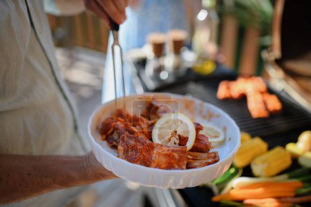 Foto de Un hombre irreconocible preparando carne y verduras para asar a la parrilla durante la fiesta familiar del jardín de verano, primer plano - Imagen libre de derechos