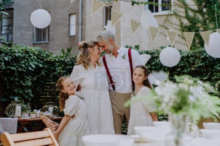 Téléchargez les photos : Mariée mature et marié posant avec leurs filles à la réception de mariage à l'extérieur dans la cour arrière. - en image libre de droit