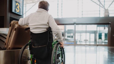 Photo for Rear view of a man on wheelchair at airport with his luggage. - Royalty Free Image