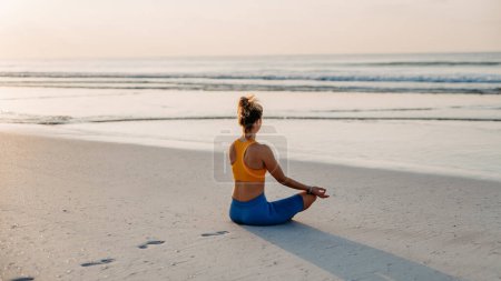 Téléchargez les photos : Vue arrière de la jeune femme faisant des exercices à la plage, routine matinale et mode de vie sain concept. - en image libre de droit