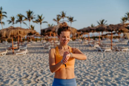 Photo for Close-up of young sportive woman at the beach, checking at smartwatch. - Royalty Free Image
