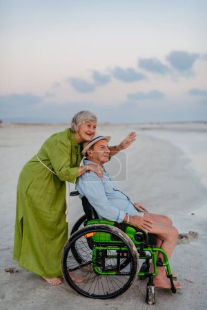 Téléchargez les photos : Homme âgé en fauteuil roulant jouissant ensemble du temps avec sa femme à la mer. - en image libre de droit