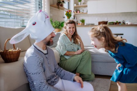 Foto de Pequeños niños divirtiéndose con su madre y su padre con máscara de conejo de Pascua, celebrando la Pascua. - Imagen libre de derechos