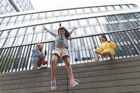 Photo for Two girls firends jumping down from concrete wall in city. Low angle view. - Royalty Free Image