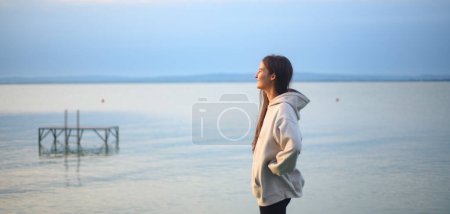 Photo for Young sportive girl standing by lake and looking at view. - Royalty Free Image