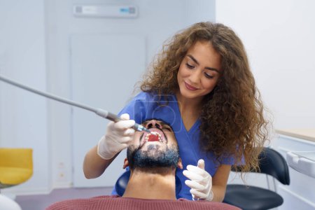Foto de Mujer joven dentista haciendo examen preventivo al hombre multirracial. - Imagen libre de derechos