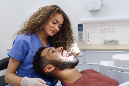 Young woman dentist doing preventive examination to the multiracial man.